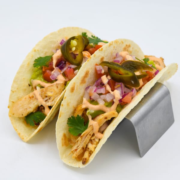 Two Cielito Lindo Mexican Food chicken tacos with guacamole, salsa, and jalapeños in a metal holder.
