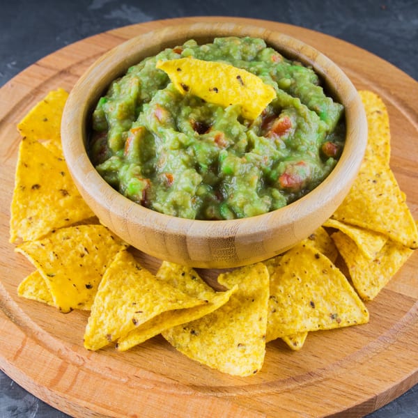 A wooden bowl of Cielito Lindo's fresh guacamole with a tortilla chip, surrounded by more chips.