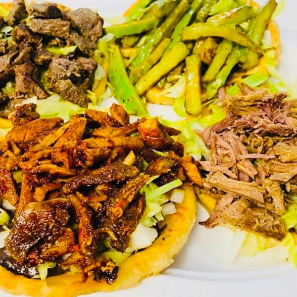 Three Mexican sopes with different meat toppings, lettuce, and green chiles on a white plate.