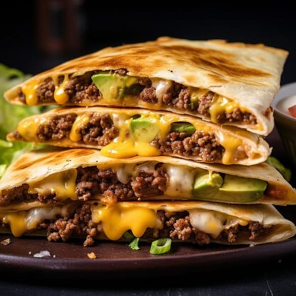Stack of three beef and cheese quesadillas with avocado slices, on a dark plate.