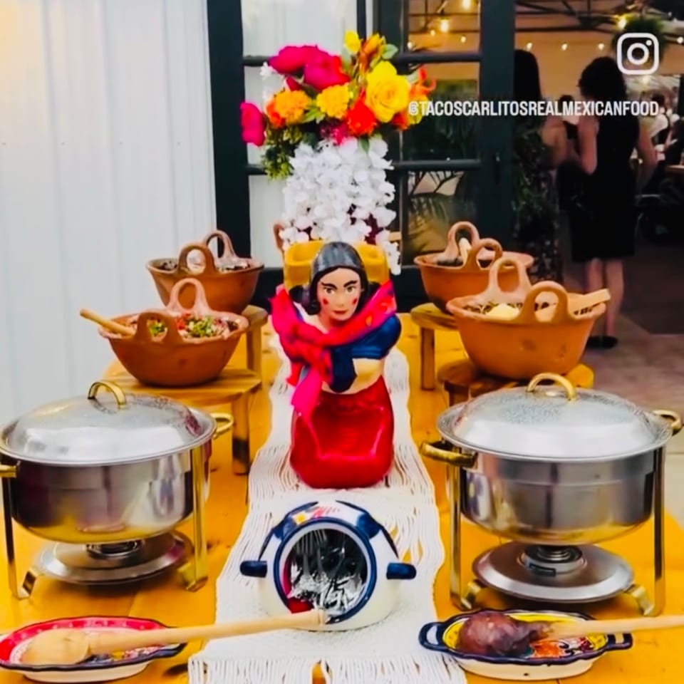 A vibrant Mexican food buffet with chafing dishes, clay bowls of food, and a Frida Kahlo statue.
