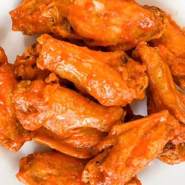 Close-up of a pile of Cielito Lindo Mexican Food's chicken wings coated in a vibrant orange sauce.