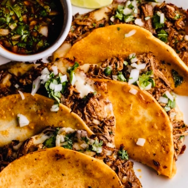 Close-up of Cielito Lindo's birria tacos with cilantro, onions, and a side of consommé.