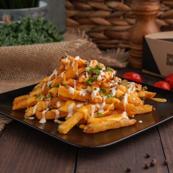 Golden french fries covered in melted cheese, white sauce, and green onions on a black plate.